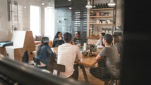Group of people in conversation around a large wooden table in a café