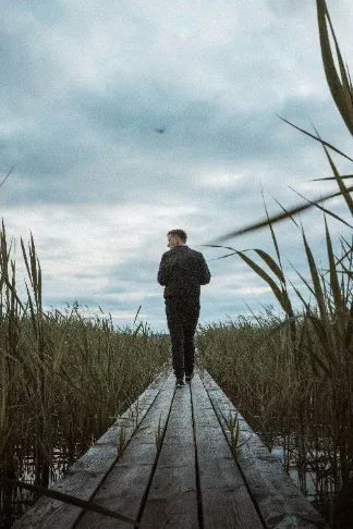 Person standing at the end of a wooden jetty leading through reeds across a lake