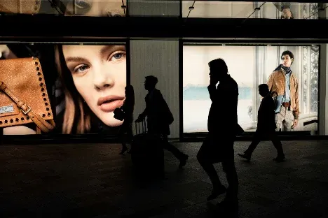 Passers-by in silhouette in front of brightly lit shop windows with fashion advertising