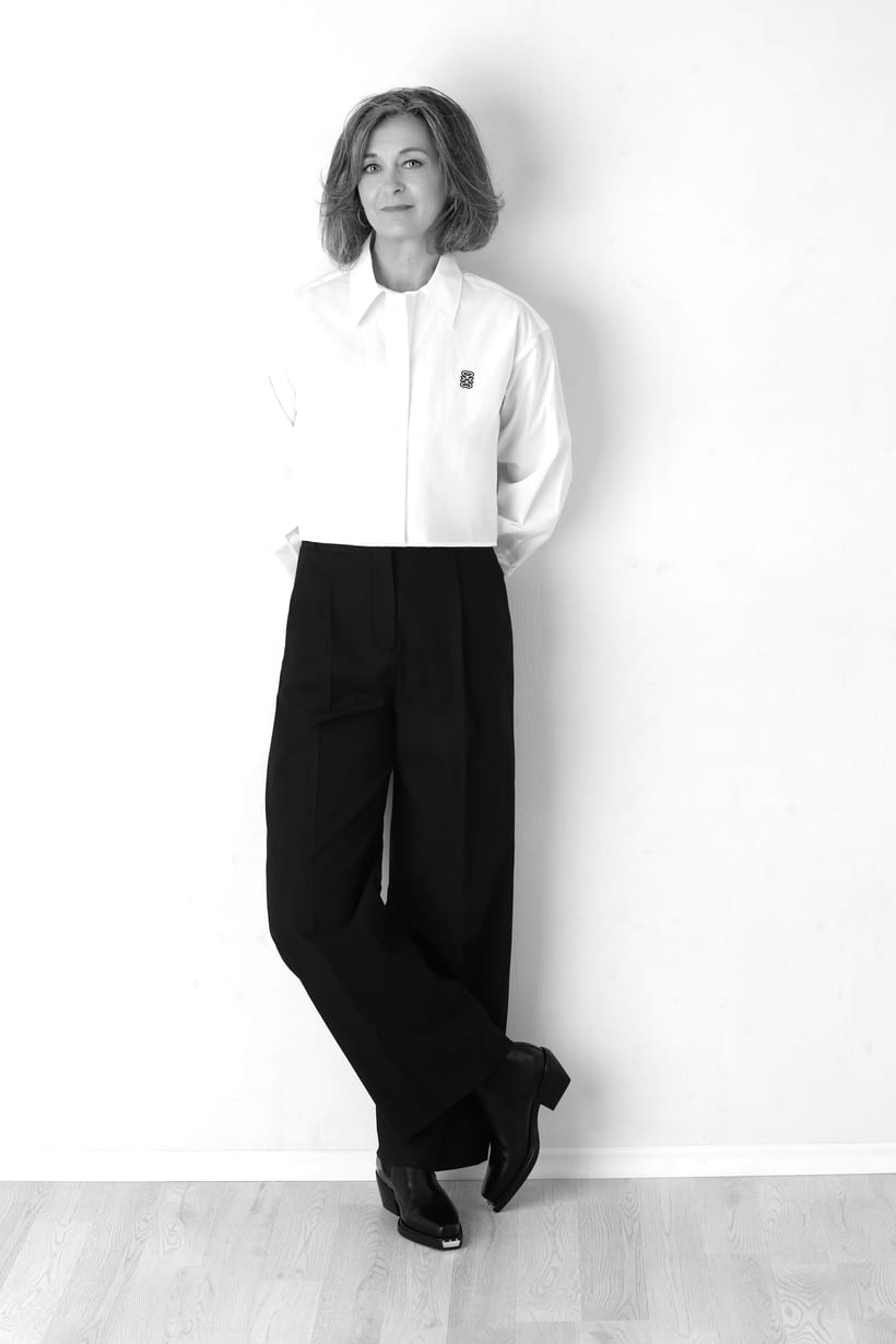A woman in a white shirt standing by a light wall.